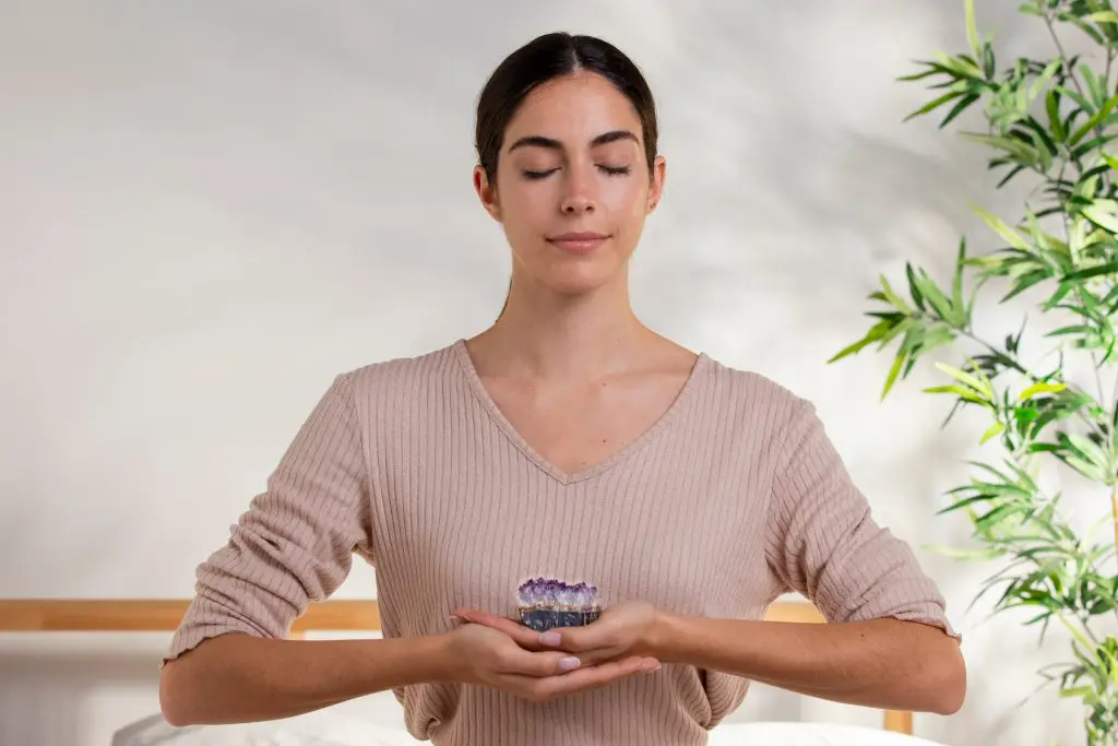 A woman holding a plant while meditating on her bed with a bedside plant