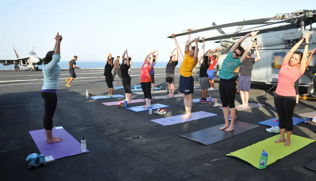 A group of service members doing yoga on a ship for exercise.