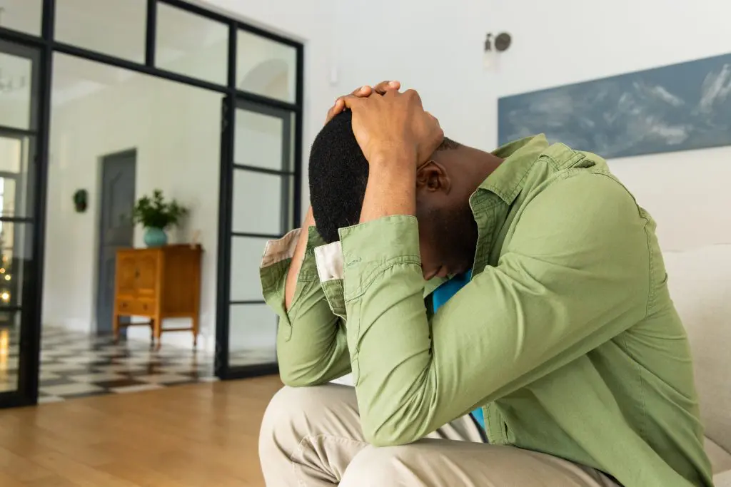 A man in a green button-down shirt sits with his head in his hands.