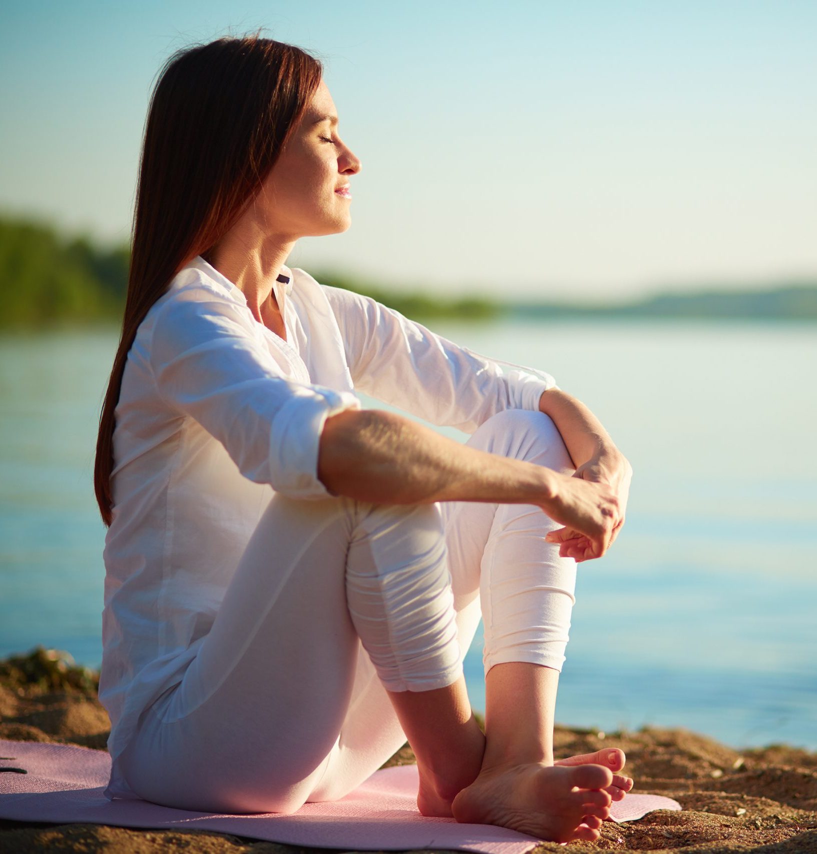 A woman sitting by the shore, feeling the breeze