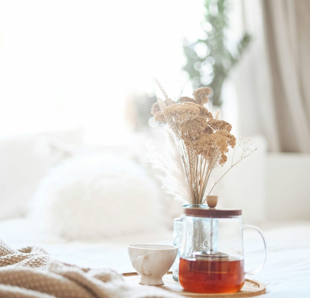 A tea set decorated with dried flowers on a bed with white sheets and brown blanket