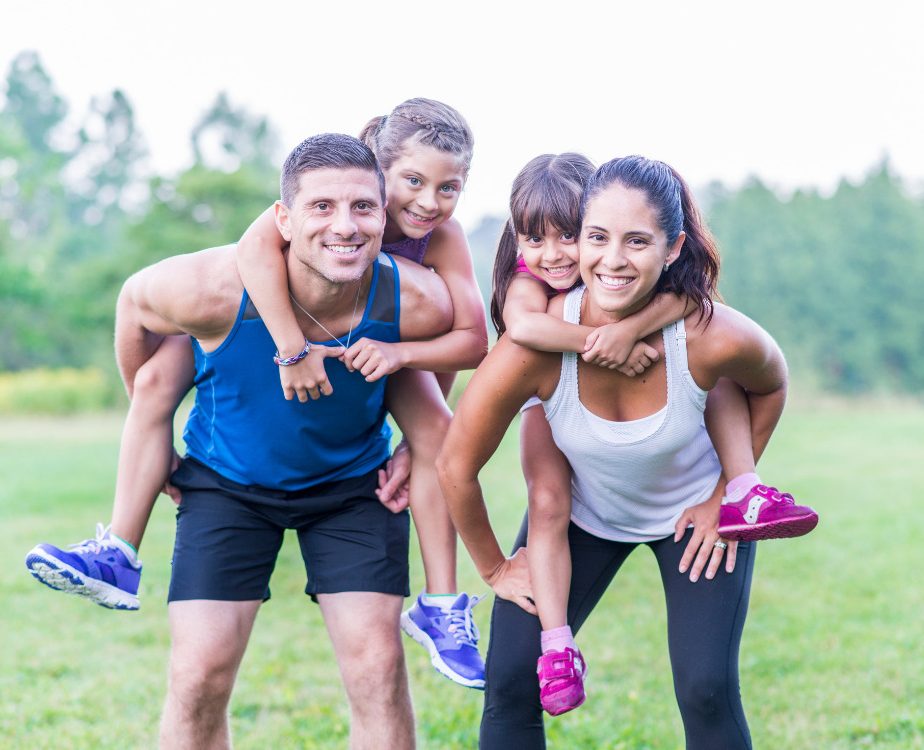 A family of four in their active wear and both kids are on each of their backs.